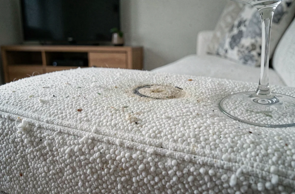 Gros plan sur un canapé blanc taché après usage en location courte durée avec verre de vin posé sur l'accoudoir