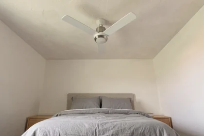 Ventilateur de plafond silencieux blanc installé dans une petite chambre à coucher minimaliste avec literie en lin gris